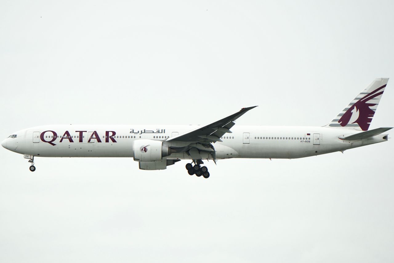 Qatar Airways airplane flying with landing gear deployed, ready for landing.